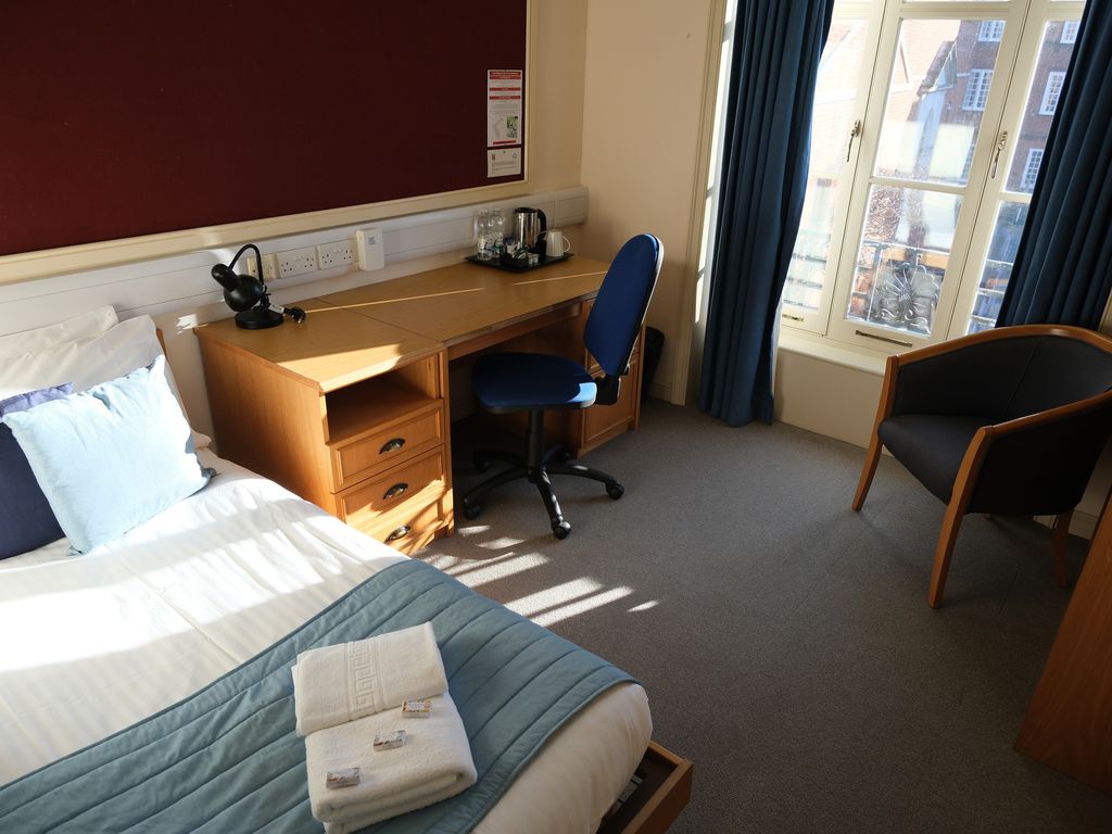 A college bedroom with a single bed, desk and armchair